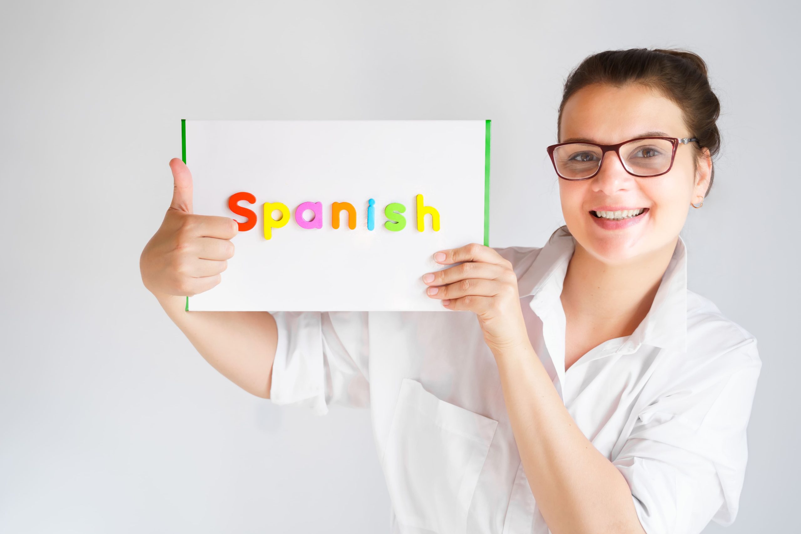 Profesora mostrando cartel de Spanish para clases de español en academia de idiomas